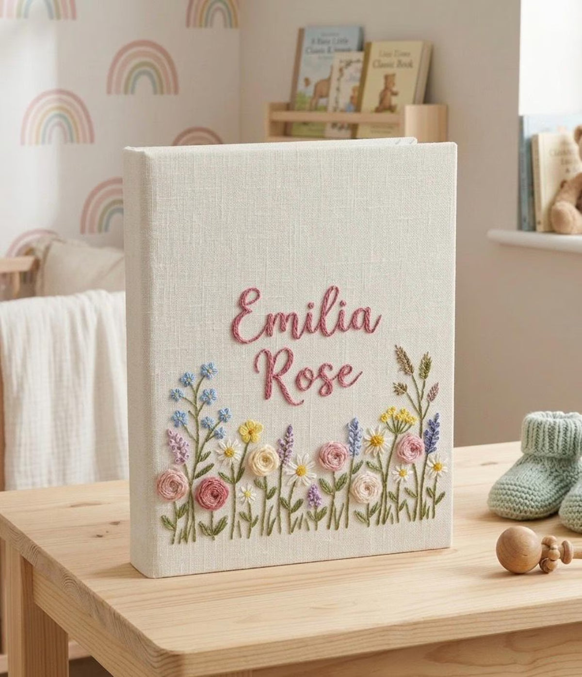 A cream-colored photo album with a name in pink script and a colorful floral design — hand-embroidered by The Thread Nest