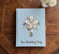 A light blue wedding guest book with an embroidered floral bouquet design — hand-embroidered by The Thread Nest