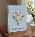 A light blue wedding guest book with an embroidered floral bouquet design — hand-embroidered by The Thread Nest