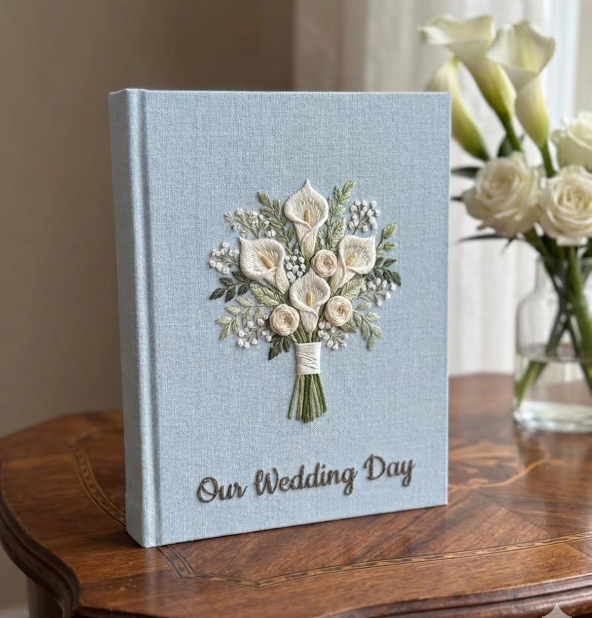 A light blue wedding guest book with an embroidered floral bouquet design — hand-embroidered by The Thread Nest