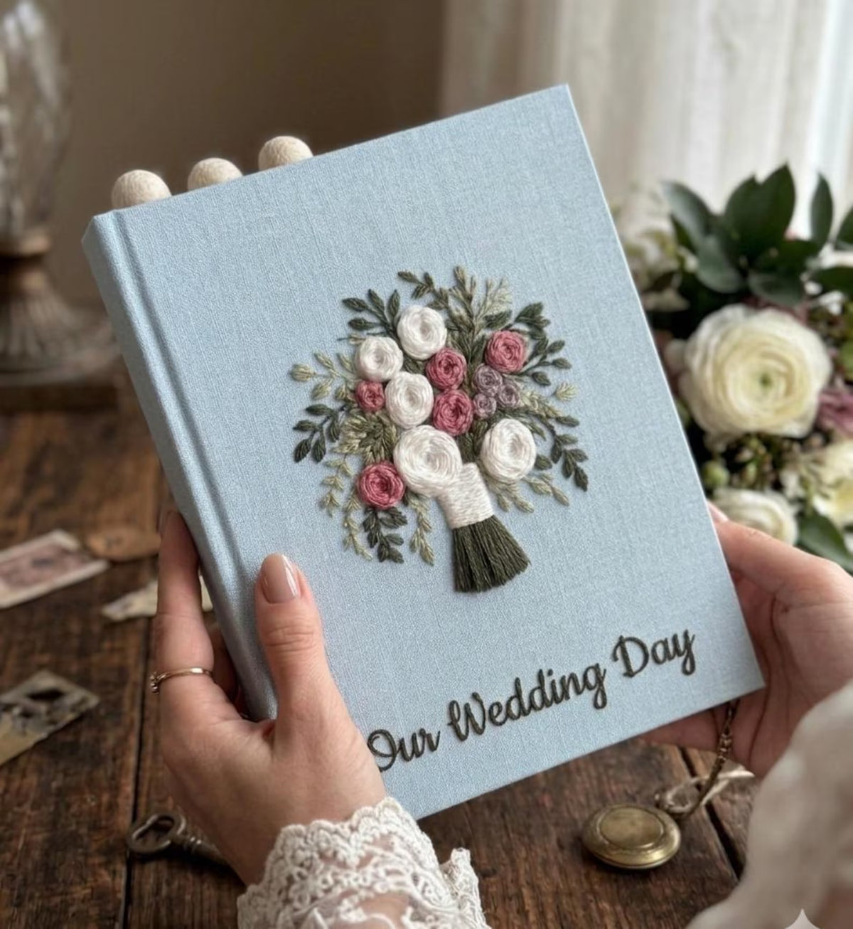 A light blue wedding journal with an embroidered floral bouquet design — hand-embroidered by The Thread Nest