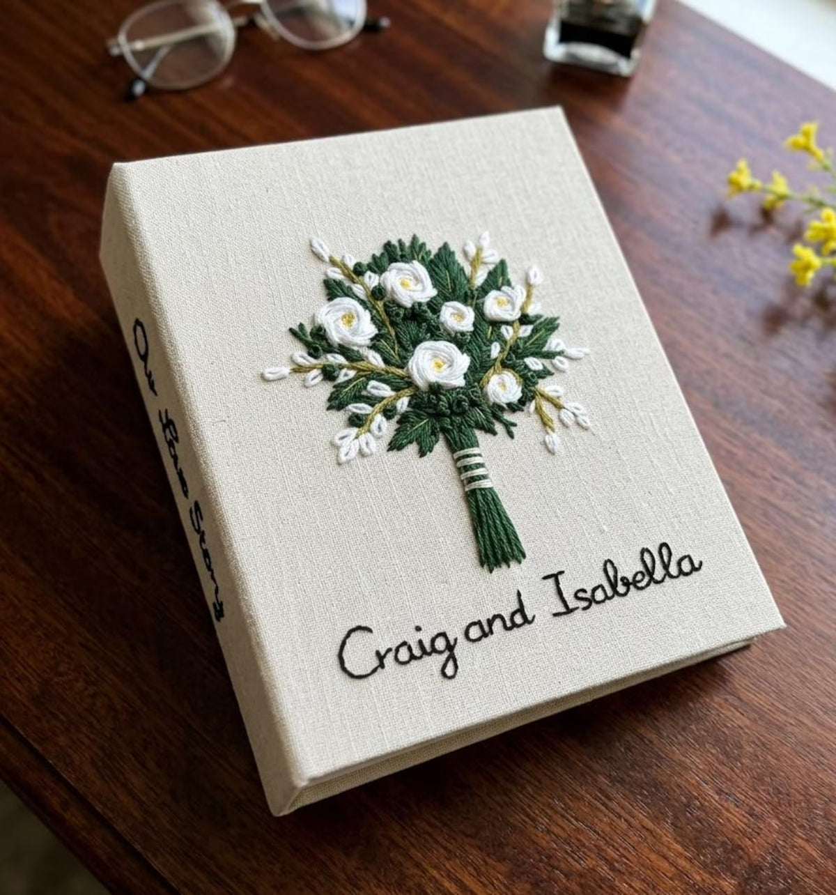 A beige fabric-covered book with an embroidered floral bouquet design — hand-embroidered by The Thread Nest