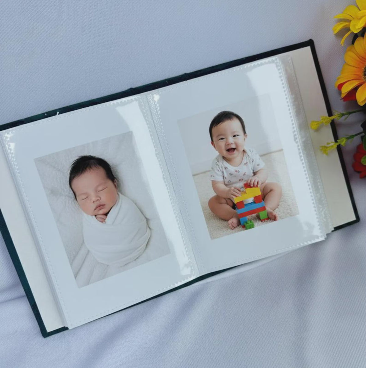 An open photo album with two baby photographs in the sleeves