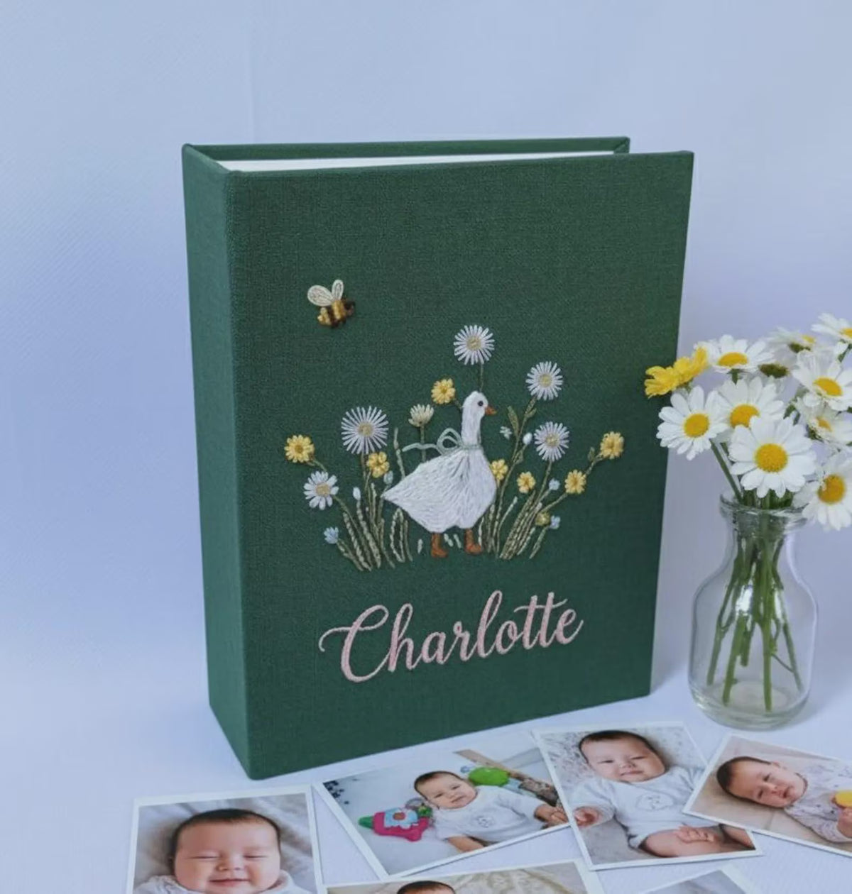 A dark green photo album with a white goose, daisies and a small bee — hand-embroidered by The Thread Nest