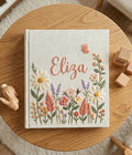 A linen-covered book with a name in cursive and a design of daisies and lavender — hand-embroidered by The Thread Nest