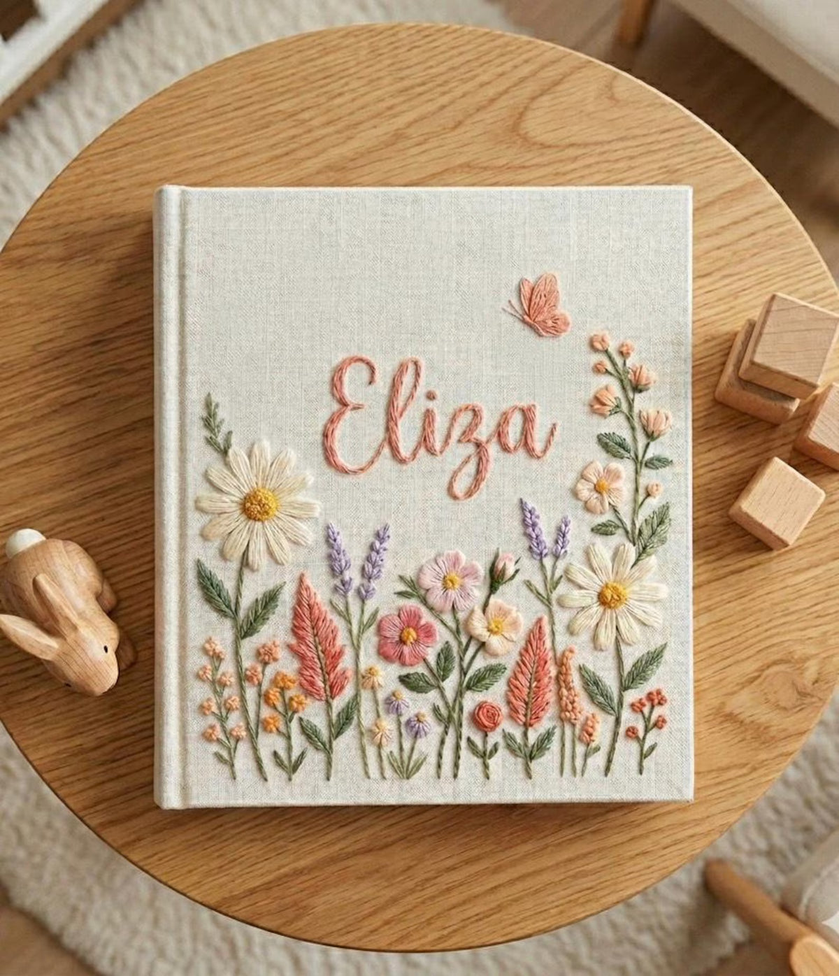 A linen-covered book with a name in cursive and a design of daisies and lavender — hand-embroidered by The Thread Nest