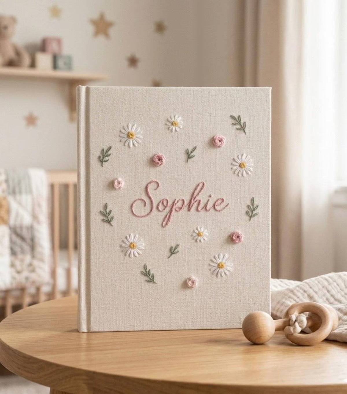 A beige linen baby memory book with daisies and small pink roses — hand-embroidered by The Thread Nest