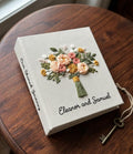 A cream-colored photo album with an embroidered floral bouquet design in peach, pink, yellow, and green — hand-embroidered by The Thread Nest