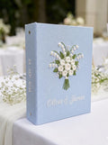 A light blue wedding guest book with an embroidered floral bouquet design — hand-embroidered by The Thread Nest