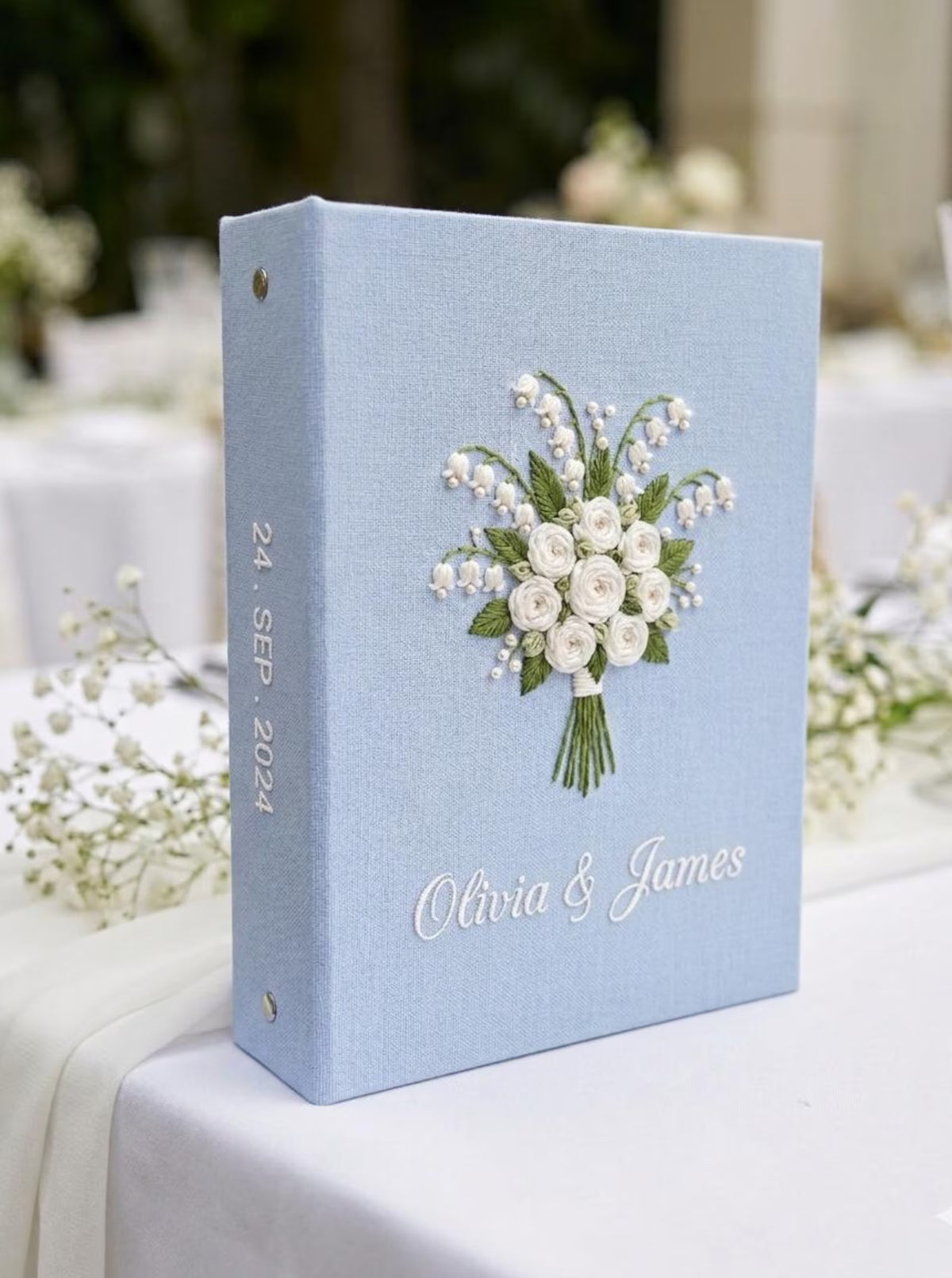 A light blue wedding guest book with an embroidered floral bouquet design — hand-embroidered by The Thread Nest