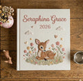 A white book with an embroidered fawn resting in a field of pastel flowers — hand-embroidered by The Thread Nest