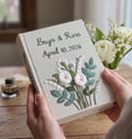 A light beige book with embroidered names, a date, and Our wedding on the spine — hand-embroidered by The Thread Nest