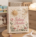 A cream-colored memory book with an embroidered sun, moon, stars and flowers — hand-embroidered by The Thread Nest