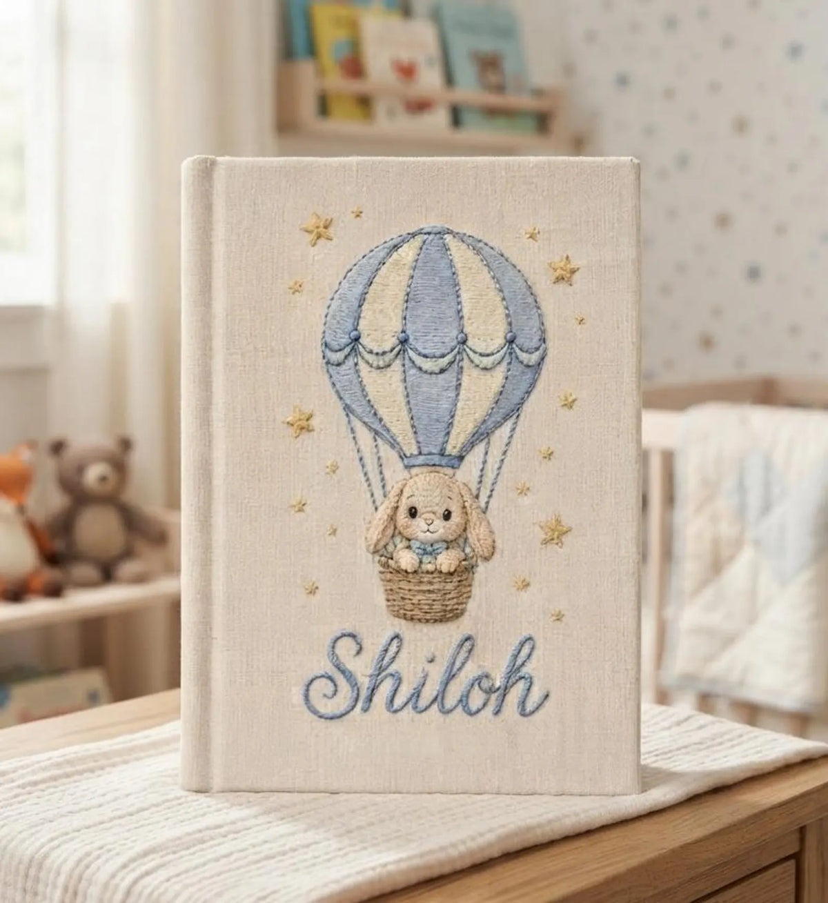 A beige book with a hot air balloon carrying a small bunny in a basket — hand-embroidered by The Thread Nest