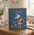A dark blue hardcover book with a rabbit in blue overalls holding balloons — hand-embroidered by The Thread Nest