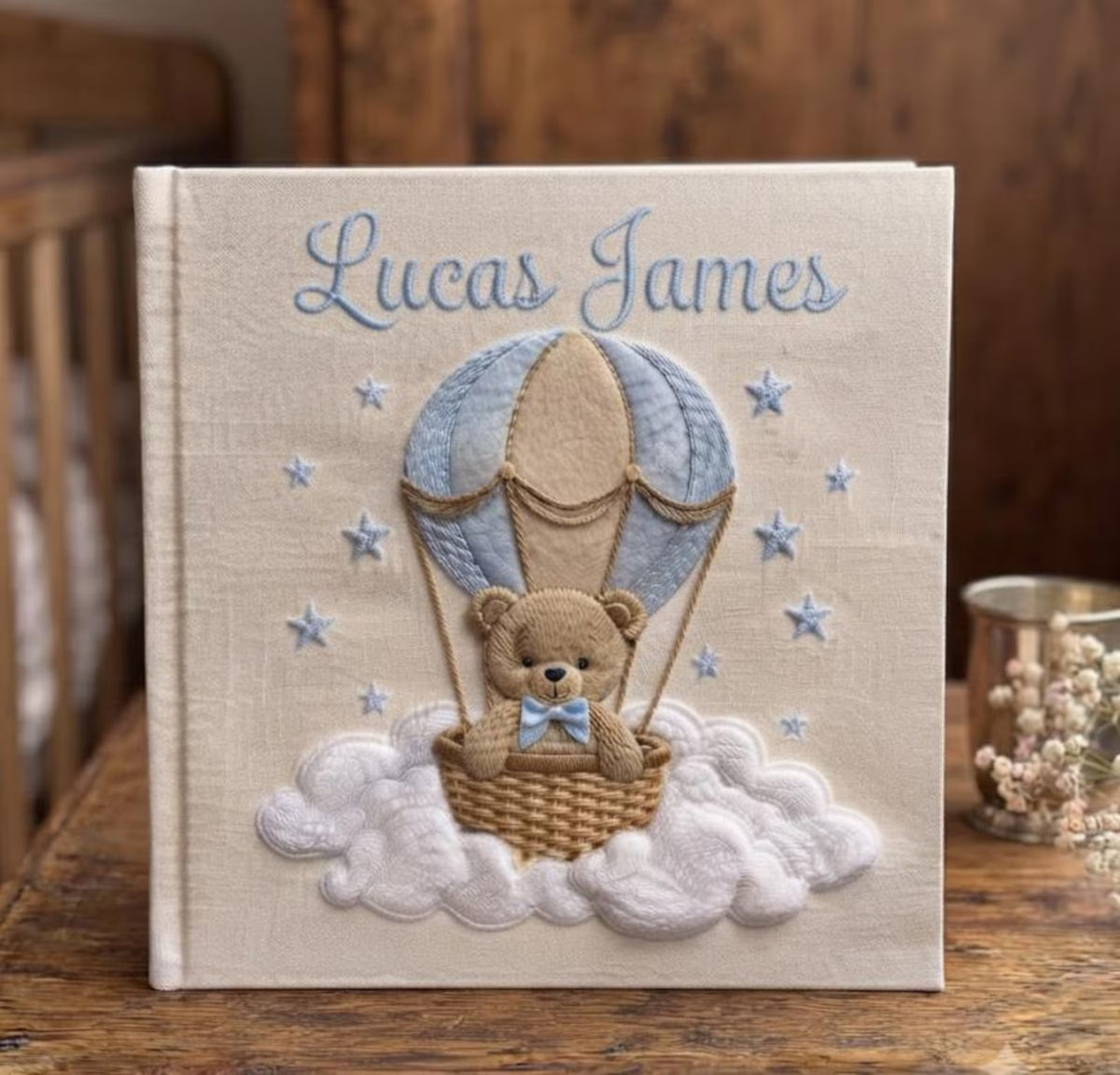 A square book with a tan teddy bear in a light blue hot air balloon — hand-embroidered by The Thread Nest