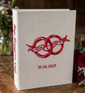 A cream-colored book with red embroidered rings and Our wedding day on the spine — hand-embroidered by The Thread Nest